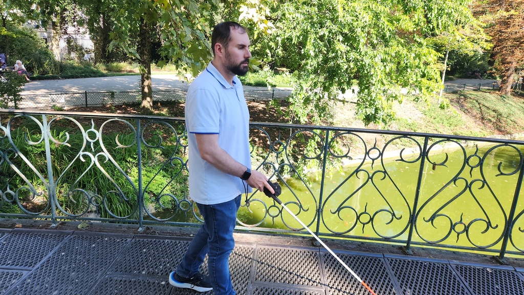 Utilisateur se déplaçant avec une canne blanche équipée de l'ICane, en extérieur près d'un plan d'eau