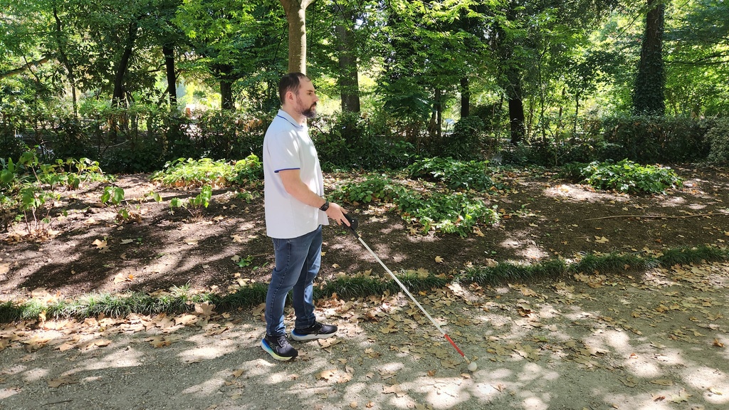 Utilisateur se déplaçant avec une canne blanche équipée de l'ICane, sur un chemin dans un parc